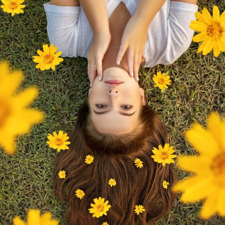 Upside down portrait of a woman lying on grass with yellow flowers in her hair.