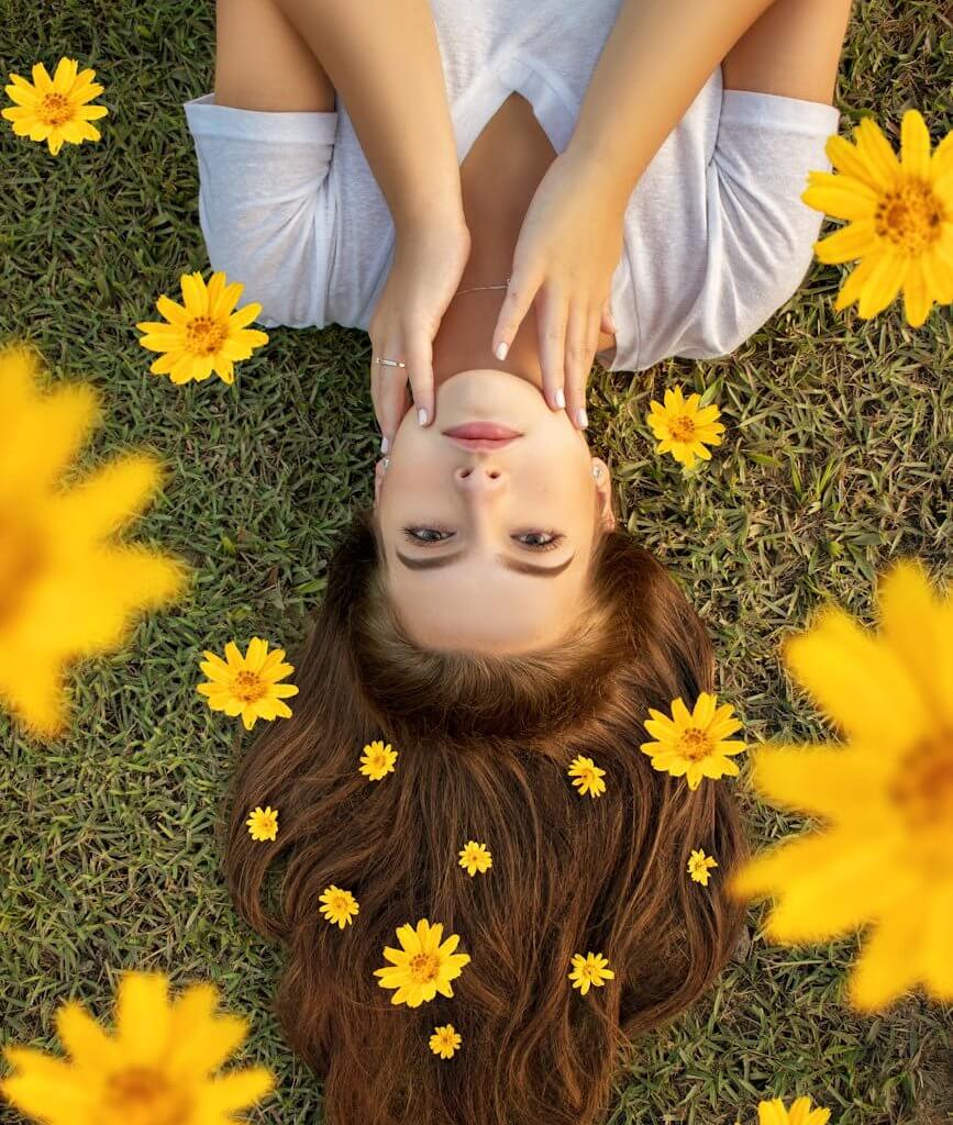 Upside down portrait of a woman lying on grass with yellow flowers in her hair.