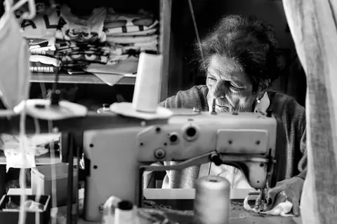 Una donna al lavoro dietro una macchina da cucire, in bianco e nero.