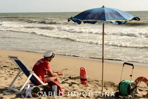Una persona seduta sulla spiaggia sotto un ombrellone blu, davanti al mare.