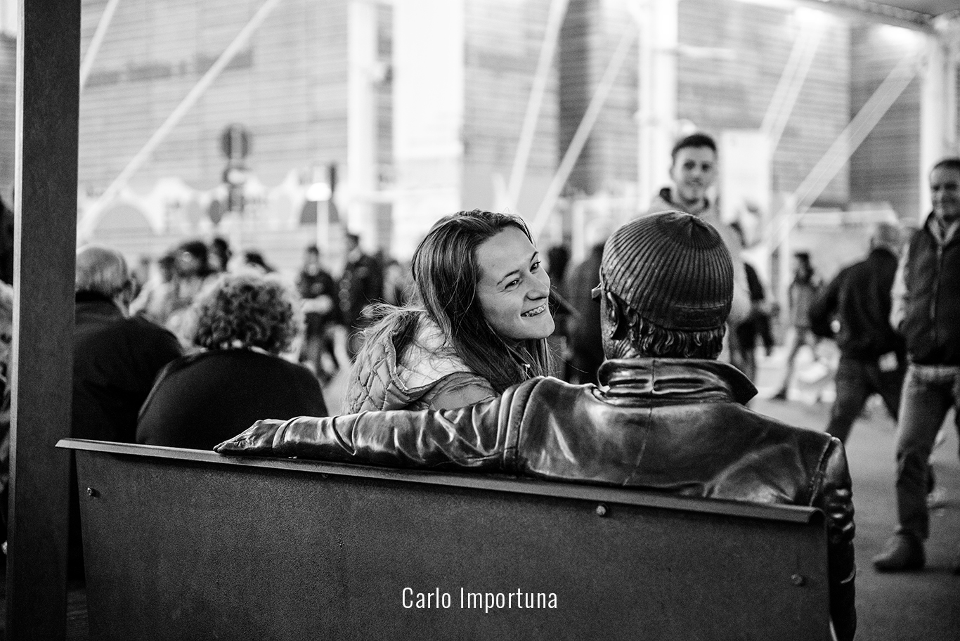 Una ragazza sorride ad una statua seduta su di una panchina Fotografia di Carlo Importuna.
